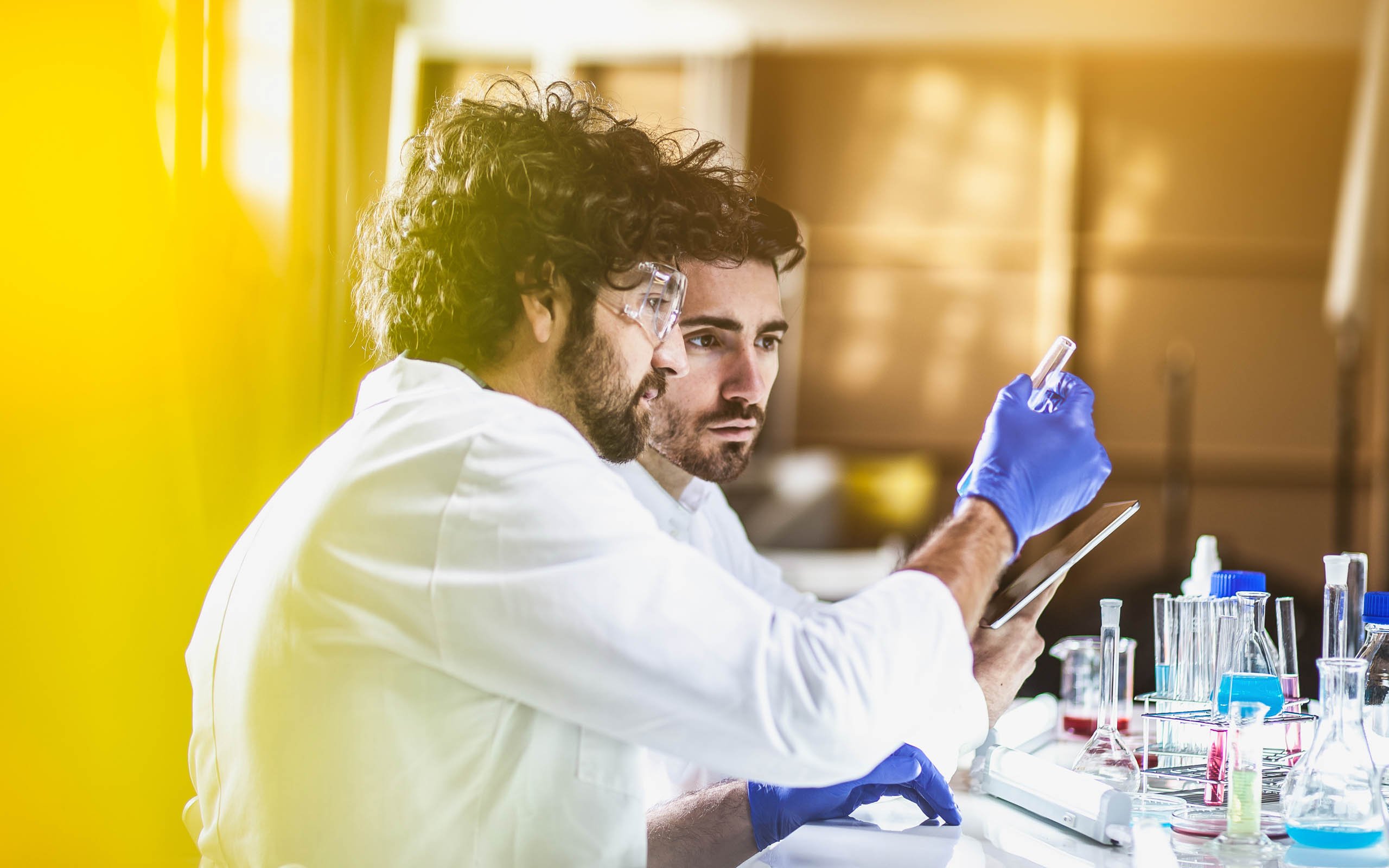 Two male scientists using cell therapy software on a tablet to record testing data.